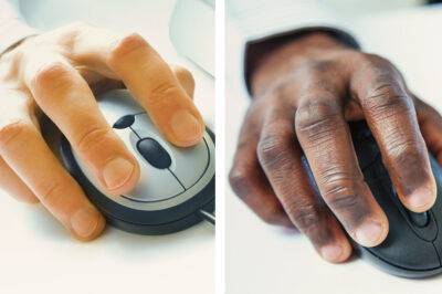 A white hand on a computer mouse side by side with a black hand on a computer mouse